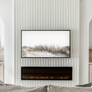 A symmetrical modern living room feature wall centered around a flat-screen TV and a sleek built-in linear electric fireplace, both mounted on a floor-to-ceiling white fluted accent panel. The center panel is flanked by identical arched alcoves containing custom light wood cabinetry and open shelving. The shelves are elegantly styled with framed artwork, dried florals, and small decor pieces, illuminated by modern white and brass wall sconces. The top edge of a light grey sofa is visible in the foreground.