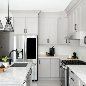 A bright, modern kitchen featuring light grey shaker-style cabinets with matte black drawer pulls and white quartz countertops with subtle grey veining. A central island houses an under-mount sink and a matte black gooseneck faucet, illuminated by two striking black wireframe pendant lights. The space is fully equipped with stainless steel appliances, including a gas range and a smart refrigerator with a built-in screen.