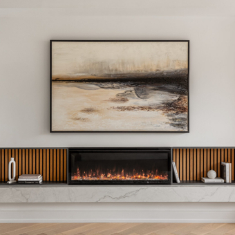 A modern living room focal point featuring a large framed abstract landscape painting in earth tones mounted above a sleek, built-in linear electric fireplace. The fireplace is symmetrically flanked by dark open shelving with vertical wood slat backings, minimally styled with books and white ceramic decor. The entire unit rests on a thick, floating white marble hearth over light wood flooring.