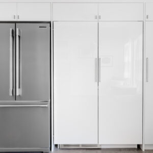 A modern, minimalist kitchen wall featuring a stainless steel French door refrigerator with a bottom freezer, positioned next to tall, glossy white flat-panel pantry cabinets. The seamless floor-to-ceiling built-in cabinetry is accented with sleek, vertical silver hardware and includes additional smaller storage compartments along the top.